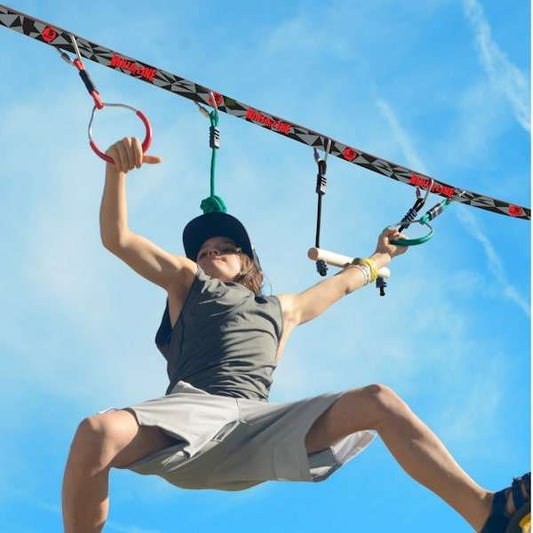 Child using Slackers Ninjaline 36' Intro Kit outdoor hanging obstacle course with rings and bars against blue sky