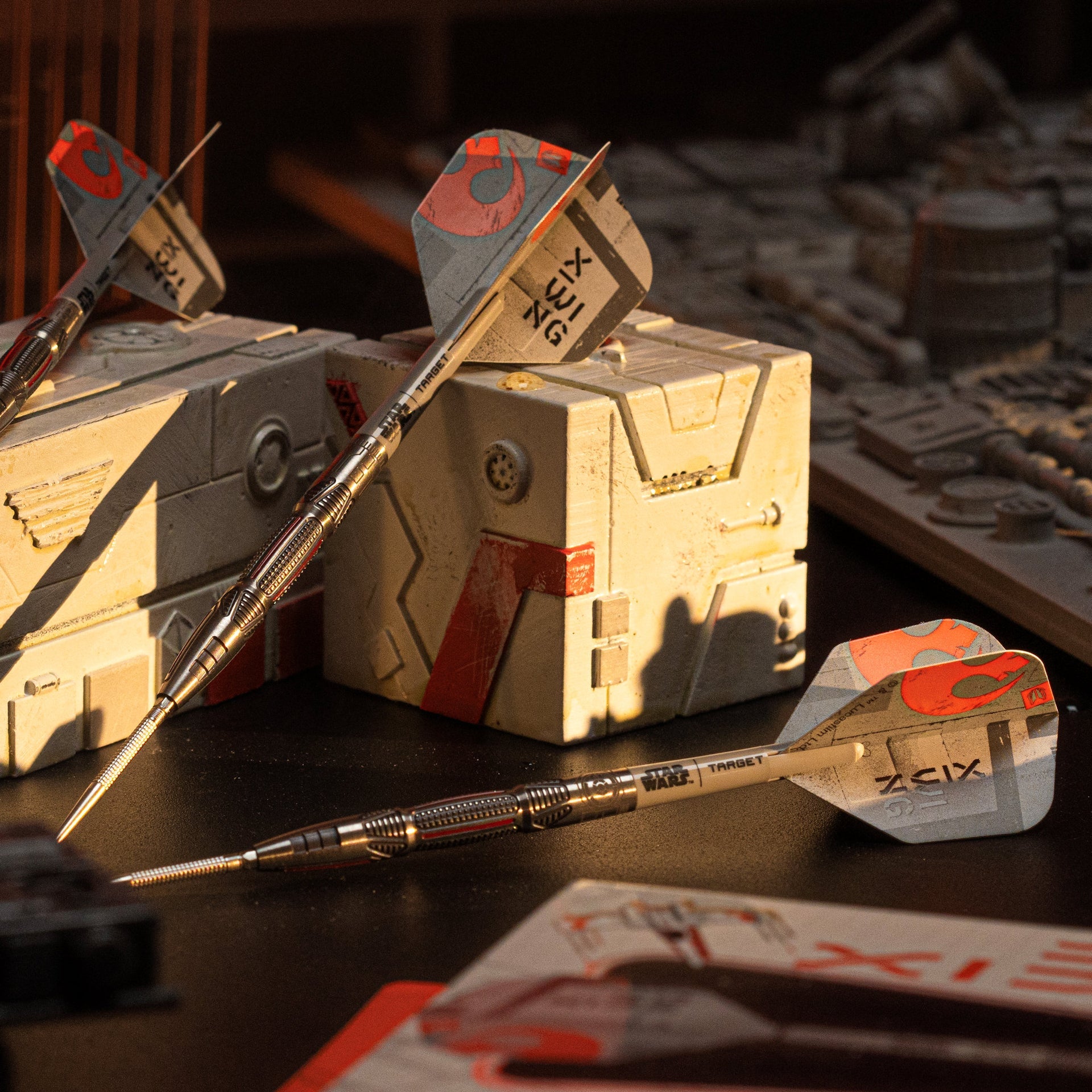 Darts with red and gray fletchings on a wooden surface with boxes in the background. Darts with red and gray fletchings on a wooden surface with boxes in the background.