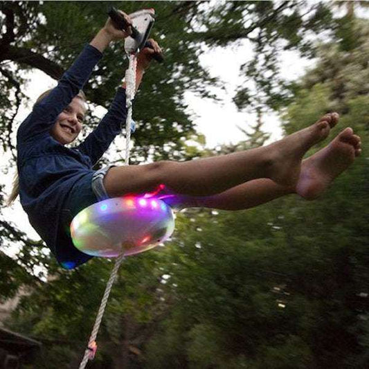 Child riding Slackers 100' Zipline with brightly lit flying saucer swing seat at dusk