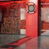 A red and black dartboard mat with the word 'TOR' printed on it, laid out on a gray tiled floor in front of a red LED wall and dartboard in a modern indoor setting.