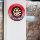 Target TOR Red Surround & dartboard with a red protective surround mounted on a white wall, flanked by stone tile walls on either side. The board is branded TARGET.
