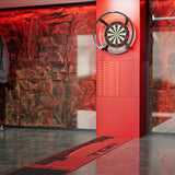 A dartboard mounted on a red pillar in a modern indoor space with a red stone-textured wall and a red runner rug on the floor.