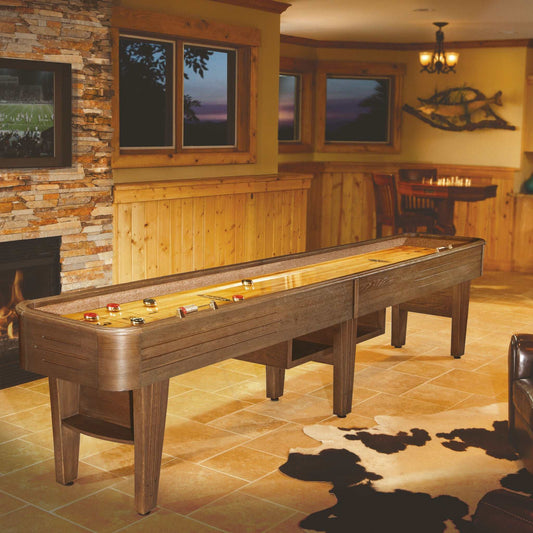 Wooden shuffleboard table in a home entertainment room with stone wall and windows.