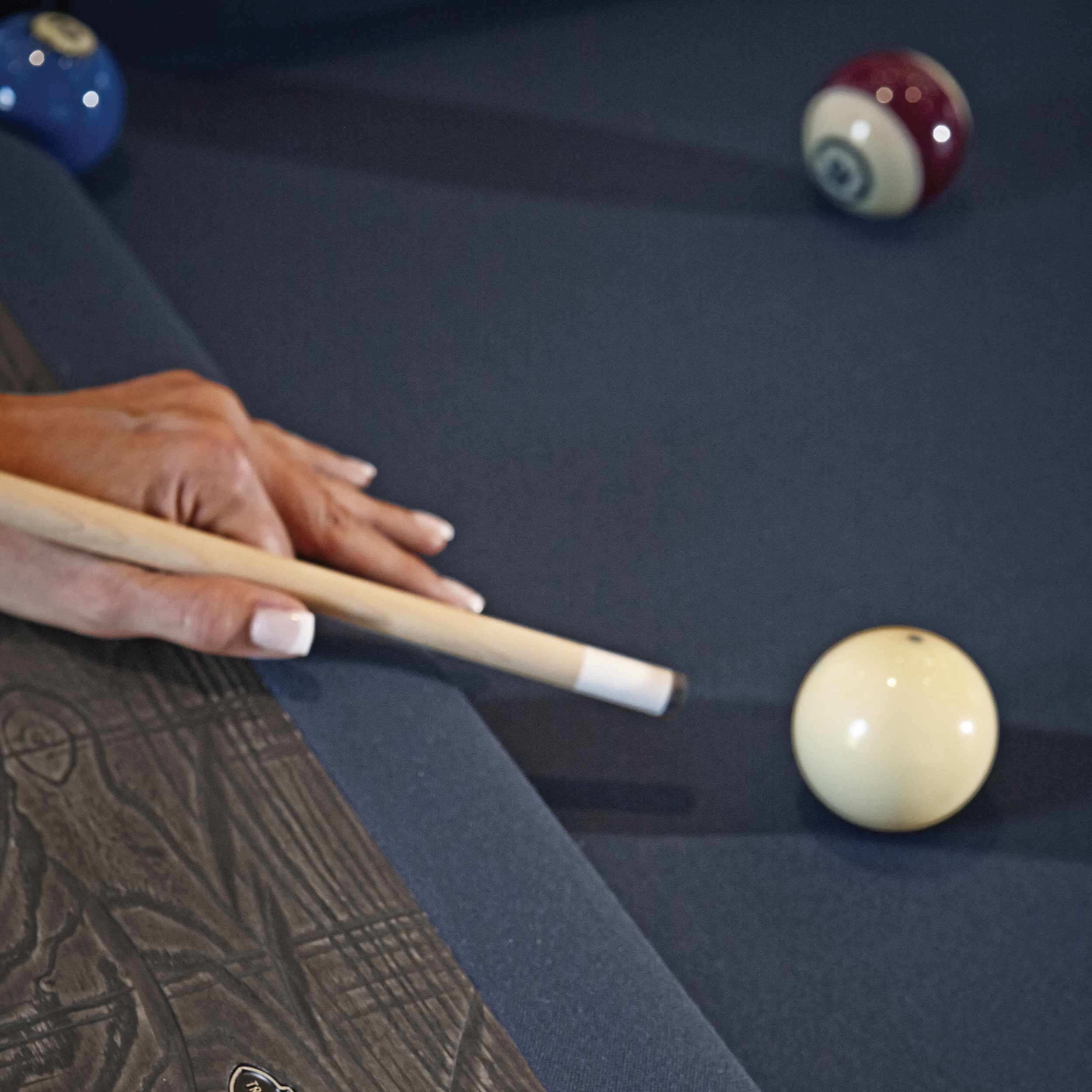 Close-up of hand aiming cue stick on navy blue cloth Birmingham Pool Table by Brunswick Billiards with rustic wood finish and billiard balls