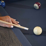 Close-up of hand aiming cue stick on navy blue cloth Birmingham Pool Table by Brunswick Billiards with rustic wood finish and billiard balls