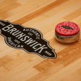 Red and silver Brunswick shuffleboard rock on a wooden surface with Brunswick logo.