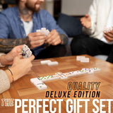 People playing a game with dominoes on a wooden table, text 'Quality Deluxe Edition The Perfect Gift Set' overlayed.