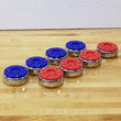 Sun-Glo Shuffleboard Rocks 2 5/16" with blue and red tops and shiny silver metal rims, arranged on a light wood shuffleboard playfield against a white wall.
