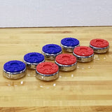 Sun-Glo Shuffleboard Rocks 2 5/16" with blue and red tops and shiny silver metal rims, arranged on a light wood shuffleboard playfield against a white wall.